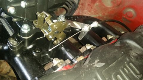 1985 Ford Bronco - A close-up view of a throttle cable mechanism attached to a black intake manifold, likely in a vehicle engine bay. The mechanism features a…