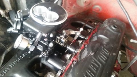 1985 Ford Bronco - A close-up view of a black aftermarket throttle body and fuel pressure gauge installed on a red engine bay. Text on the intake manifold rea…