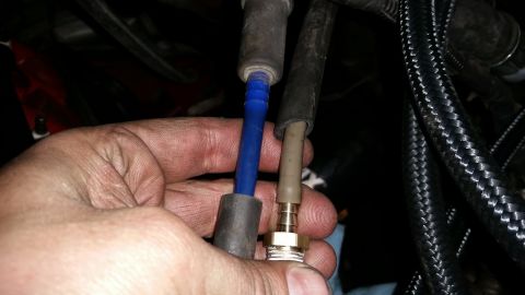 1985 Ford Bronco - A person's hand holds two spark plug wires, one blue and one tan, near the engine bay of a vehicle. The wires are connected to what appear…