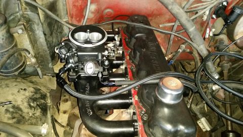 1985 Ford Bronco - A close-up view of a modified engine bay, focusing on a black carburetor and intake manifold assembly. Braided fuel lines and various hoses…
