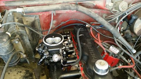 1985 Ford Bronco - Engine bay of a red vehicle showing a V8 with twin-bore throttle body, red plug wires and intake manifold.