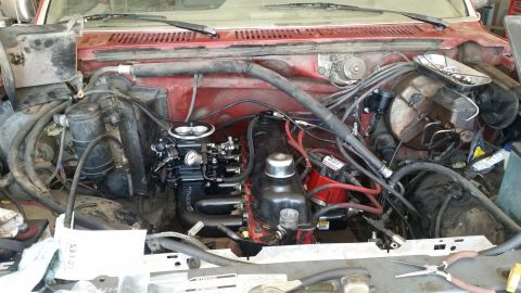 1985 Ford Bronco - A close-up view of a red Ford Bronco's engine bay, showing a newly installed black carburetor and red engine components.