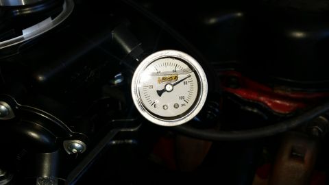 1985 Ford Bronco - A close-up of a silver gauge with black markings and a needle pointing to approximately 45 PSI. The gauge is mounted on a black component,…