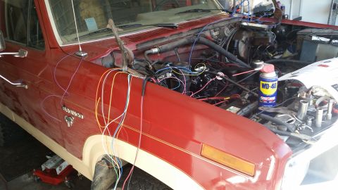 1985 Ford Bronco - The front fender and engine bay of a red Ford Bronco are shown with a large amount of wiring exposed. A can of WD-40 and various tools are…