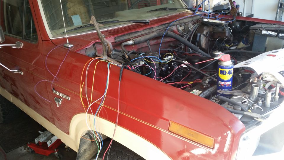 Red Ford Bronco with exposed wiring and tools in the engine bay.