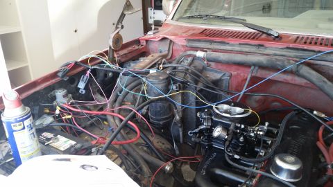 1985 Ford Bronco - The engine bay of a red Ford Bronco is shown with various wires and engine components exposed. A battery, a can of WD-40, and a carburetor…