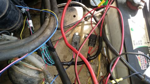1985 Ford Bronco - A close-up view of a vehicle's engine bay wiring harness, featuring a battery, circuit breaker, and various colored wires connected to comp…
