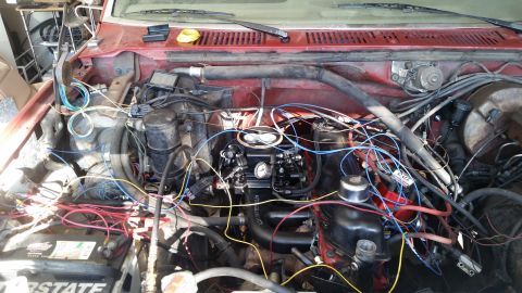 1985 Ford Bronco - The engine bay of a red 1985 Ford Bronco shows a complex wiring harness connected to the carburetor and other engine components. The vehicl…
