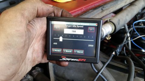 1985 Ford Bronco - A hand holds a Holley Sniper EFI digital display showing an initial wizard setup for target idle speed at 750 RPM. The display is positione…