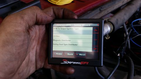 1985 Ford Bronco - A hand with dirty fingers holds a Holley Sniper EFI digital display unit, showing an initial wizard screen with options for RPM to Sniper/I…
