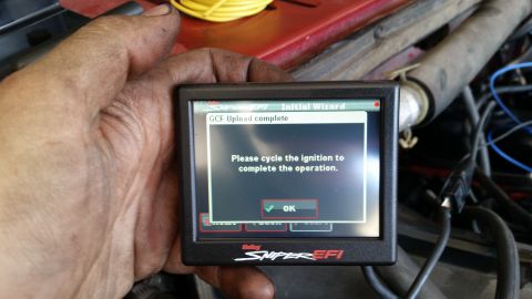 1985 Ford Bronco - A person's dirty hand holds a Holley Sniper EFI digital display showing a "GCF Upload complete" message and instructions to cycle the ignit…