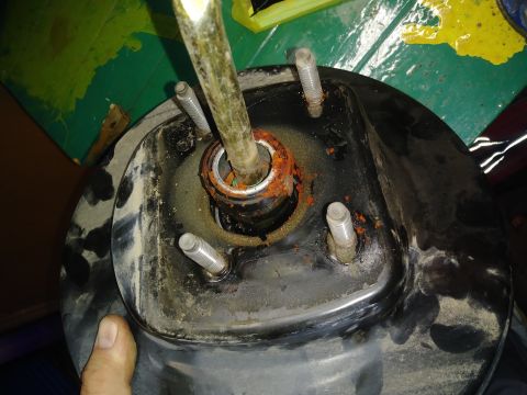 1996 Ford Bronco - A close-up view of a brake booster with a metal rod extending from the center. Rust is visible around the rod and on the mounting studs.