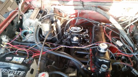 1985 Ford Bronco - A close-up, overhead view of a red vehicle's engine bay, showing a black carburetor, red engine block, and various wires and hoses. A car b…