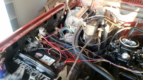 1985 Ford Bronco - The engine bay of a red 1985 Ford Bronco shows a detailed view of the battery, wiring harness, and carburetor. Various colored wires are vi…