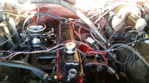 1985 Ford Bronco - A close-up view of a red engine bay, focusing on the carburetor, valve cover, and various hoses and wires. The engine appears to be a V8 wi…