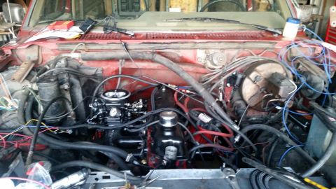1985 Ford Bronco - The engine bay of a red 1985 Ford Bronco is shown, featuring a newly installed black carburetor and various engine components with numerous…