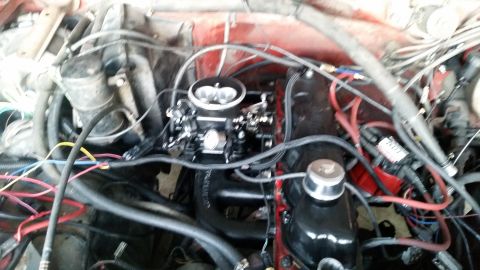 1985 Ford Bronco - The image shows a close-up view of an engine bay, likely from a classic Ford Bronco. A prominent carburetor sits atop the engine, surrounde…