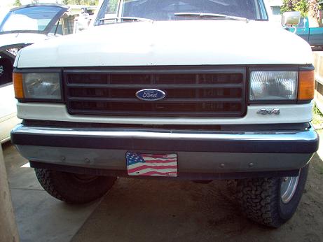 1988 Ford Bronco - Front view of a white Ford truck, a black grille and an American flag license plate.