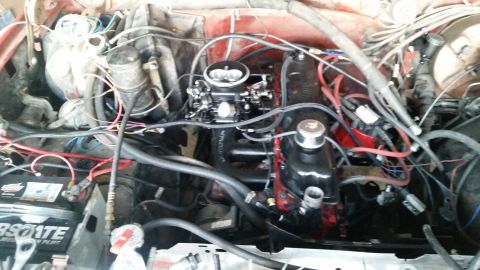 1985 Ford Bronco - A close-up view of a red vehicle's engine bay, featuring a black carburetor, red engine components, and numerous wires and hoses.