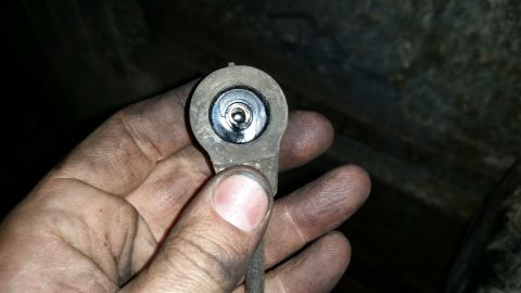 1985 Ford Bronco - A dirty hand holds a close-up of a small, round, gray automotive sensor with a black, circular opening containing a metallic component.