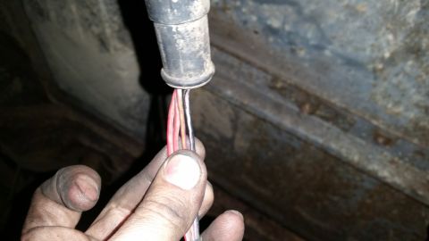 1985 Ford Bronco - A person's dirty hands hold a bundle of colorful wires emerging from a black conduit. The background appears to be the underside of a vehic…