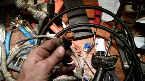 1985 Ford Bronco - A hand holds a dirty electrical connector with a ribbed grey wire attached. Various tools, including a torque wrench and pliers, are scatte…