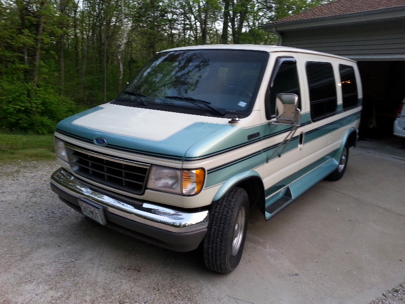 Cream and teal Ford Econoline van parked on gravel driveway.