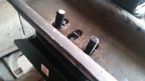 1985 Ford Bronco - Two threaded bolts are visible, protruding through a metal bracket that is attached to a larger, rusty metal component. The bolts are secur…