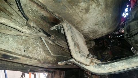1985 Ford Bronco - The underside of a vehicle shows a fuel tank and a metal bracket bolted to the frame. Various hoses and wires are visible, along with surfa…
