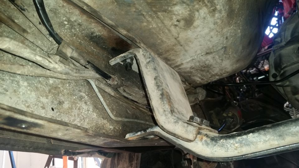 Underside of a vehicle showing fuel tank, bracket, hoses, and wires.
