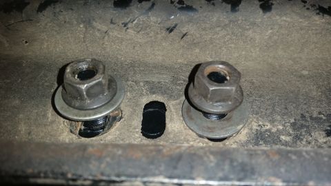 1985 Ford Bronco - Two bolts with washers and nuts are secured through a metal bracket. A dark, oblong hole is visible between the two bolts.