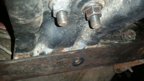 1985 Ford Bronco - This close-up photo shows rusty metal components and bolts, likely from the undercarriage of a vehicle. A black hose or cable is visible in…