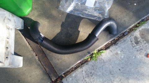 1985 Ford Bronco - A black flexible hose with ribbed texture is laid out on a concrete surface next to a white plastic container and a green jug. The hose has…