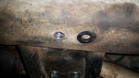 1985 Ford Bronco - A close-up view shows two holes drilled into a rusty, heavily soiled metal component, likely part of a vehicle's undercarriage. One hole is…