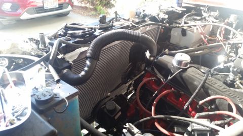 1985 Ford Bronco - Close-up view of a vehicle's engine bay, showing the radiator, hoses, and engine components. A red vehicle is partially visible in the back…
