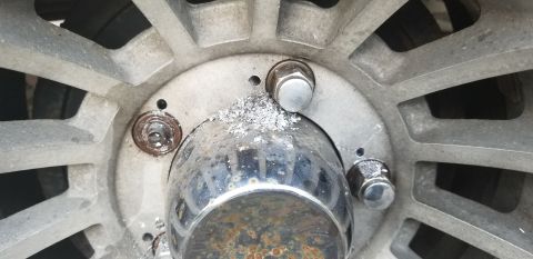 1995 Ford Bronco - A close-up view of a vehicle's wheel hub shows multiple lug nuts, a chrome center cap with rust, and some aluminum shavings around the hub.
