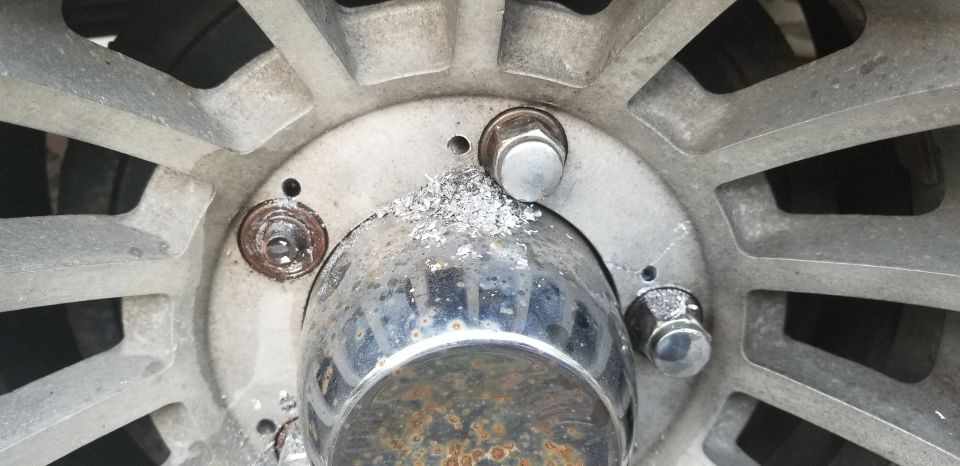 Close-up of a vehicle wheel hub with lug nuts, chrome center cap, and aluminum shavings.