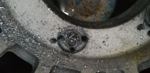 1995 Ford Bronco - A close-up view of a damaged metal component, possibly a wheel hub or brake rotor, showing significant wear, debris, and a broken bolt or s…