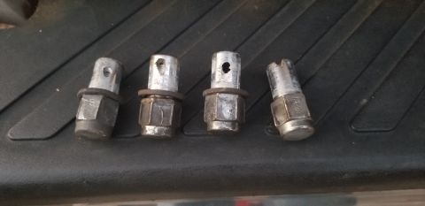 1995 Ford Bronco - Four lug nuts with integrated wheel locks are laid out on a black textured surface. One lug nut has visible text that reads "12-21".