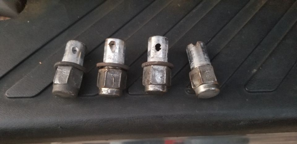 Four lug nuts with integrated wheel locks on a black textured surface.