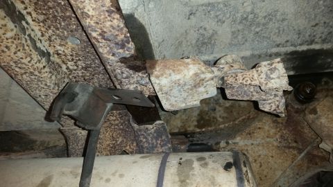 1985 Ford Bronco - The underside of a vehicle shows heavily rusted metal frame components and what appears to be part of the exhaust system. Several metal bra…
