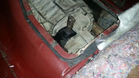 1985 Ford Bronco - Close-up view of a vehicle's transmission tunnel with a black aftermarket transmission mount visible. The red interior body panel and grey…