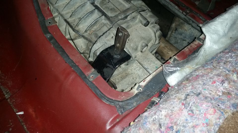 Vehicle transmission tunnel with aftermarket mount and red interior panel.
