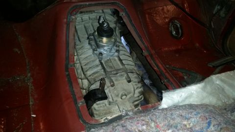 1985 Ford Bronco - The interior of a vehicle shows a manual transmission shifter and gearbox assembly installed in the center console area. Red painted metal…