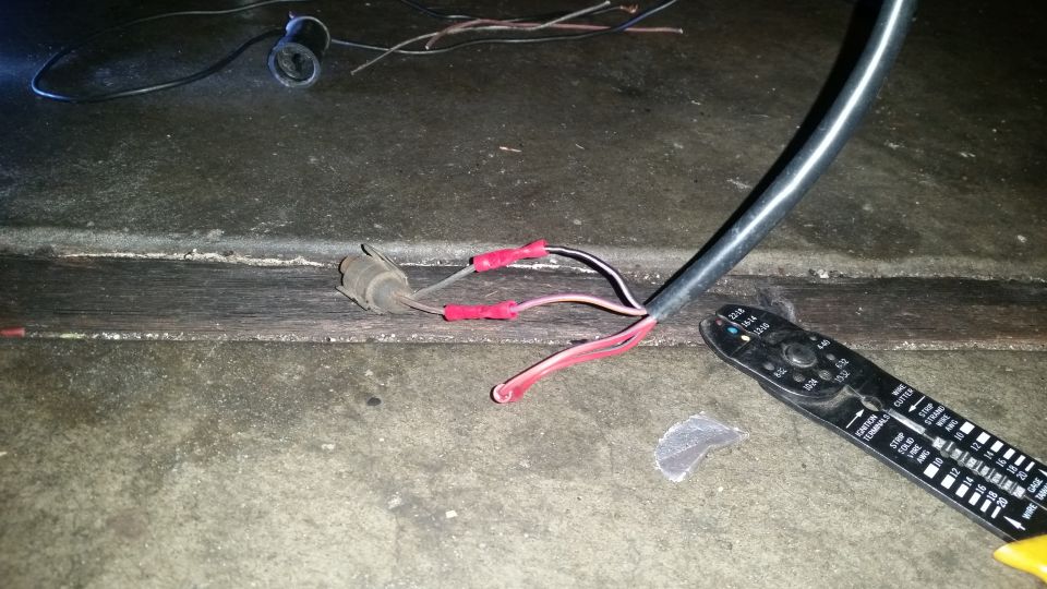 Electrical wiring with red connectors and a wire stripper tool on a concrete surface.