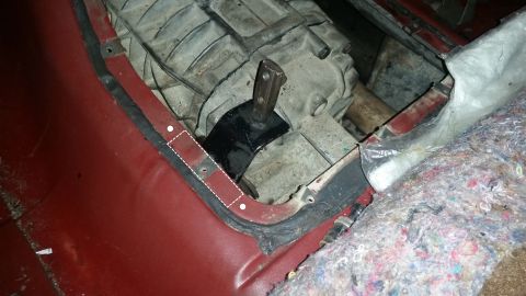 1985 Ford Bronco - A close-up view of a vehicle's transmission tunnel area, showing the transmission, a black metal bracket, and red painted metal with a blac…