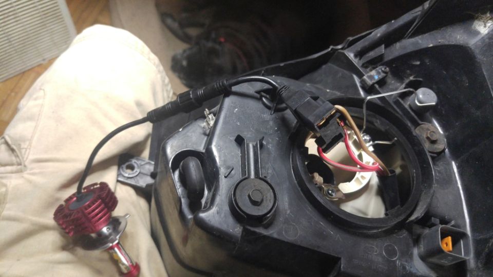 Aftermarket LED bulb connected to a headlight assembly on a person's lap.