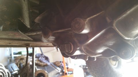 1985 Ford Bronco - The underside of a vehicle, showing the transmission or transfer case with a square plug visible. The vehicle appears to be on a lift or ja…
