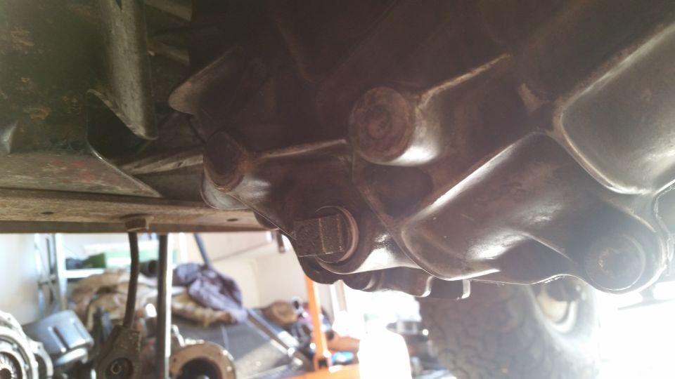 Underside of a vehicle showing transmission/transfer case and a square plug.