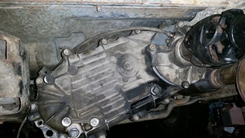1985 Ford Bronco - The underside of a vehicle shows a transfer case and part of a driveshaft. The transfer case is a complex metal component with multiple bol…